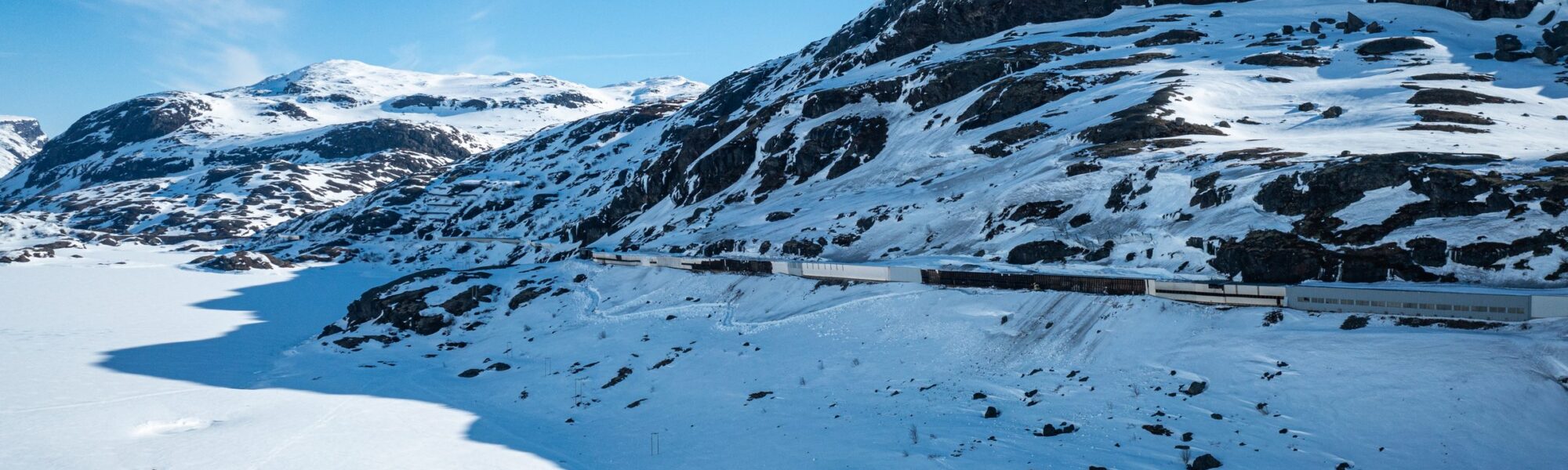 Bergensbanen som en tynn linje gjennom snødekt høyfjell, sett fra lufta