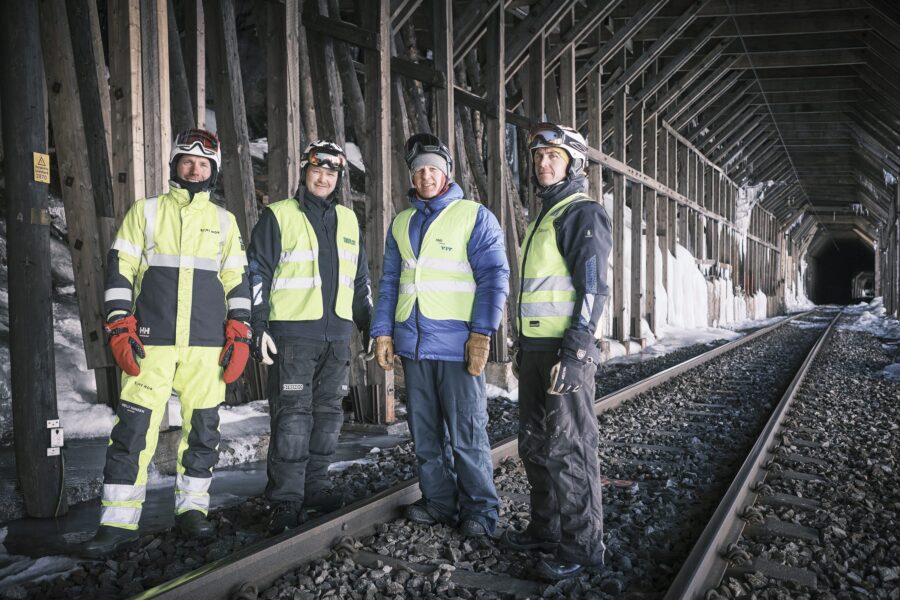Fire personer i arbeidsklær og hjelm står på sporet inne i snøoverbygget