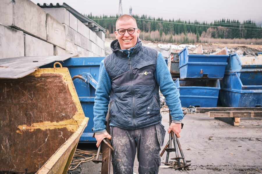 Smilende mann i arbeidsklær foran containere på et avfallsmottak
